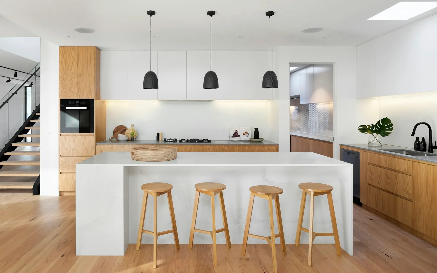 Cuisine claire avec îlot central, tabourets en bois et suspensions noires