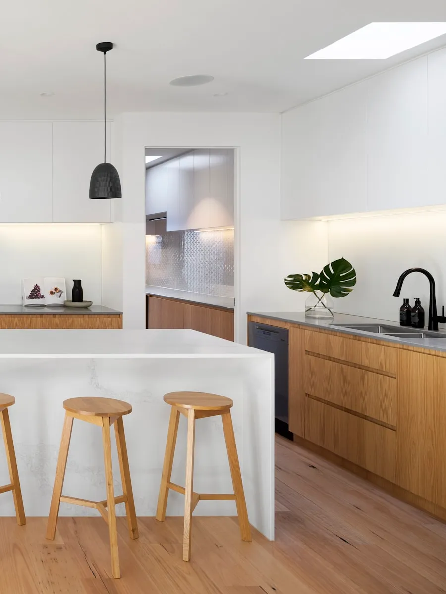 Cuisine claire avec îlot central, tabourets en bois et suspensions noires